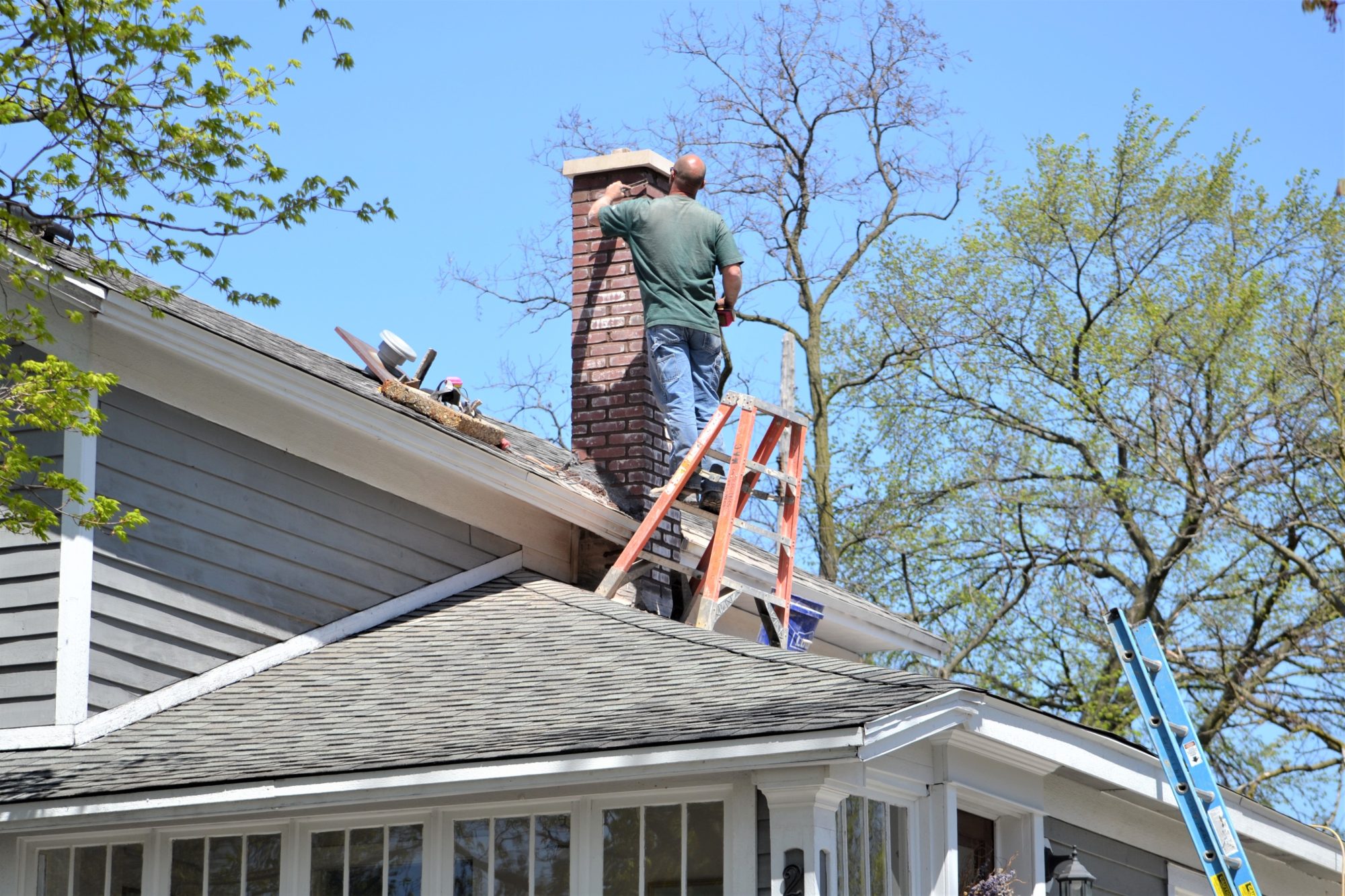 Technician standing on a roof working on a chimney with a ladder nearby